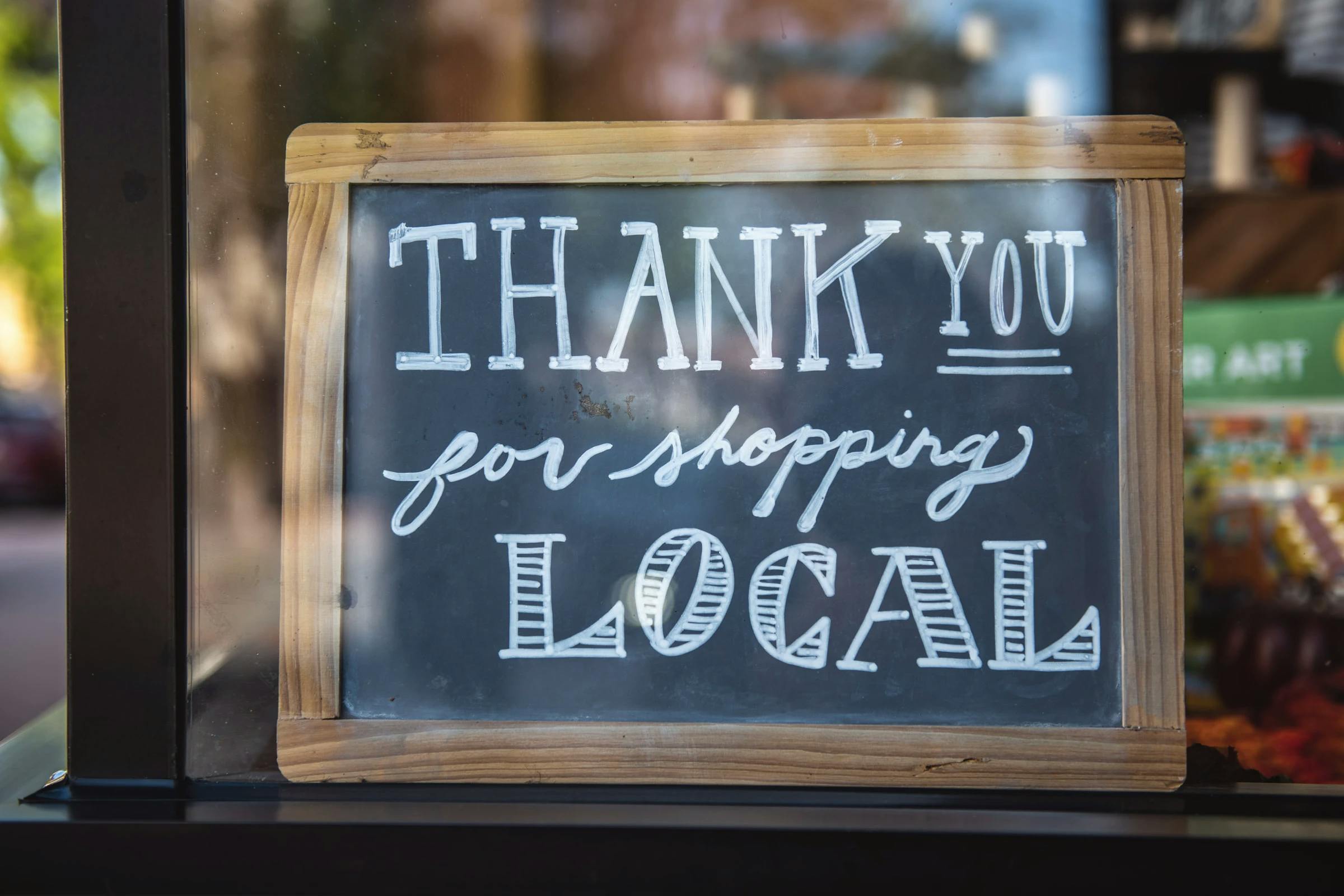 Un panneau au travers la vitrine d'un magasin affichant "Thank you for shopping local"